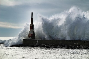 Obraz premium Giant waves breaking on the breakwater and the lighthouse