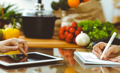 Close-up of human hands using tablet or touch pad. Two women in kitchen. Cooking, friendship or family fun concepts