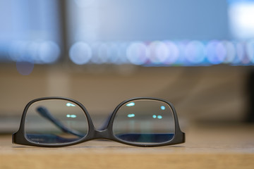 Closeup of protective glasses on an empty desk with blurred computer screen on background.