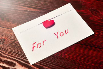 White envelope with a heart and an inscription for you on a dark wooden background.