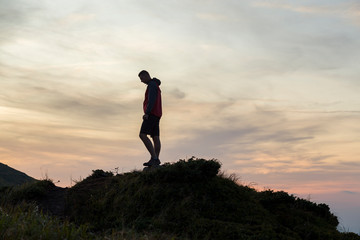 Dark silhouette of a hiker on a mountain at sunset standing on summit like a winner.