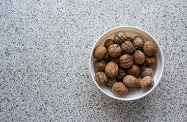 Top view Inshell walnuts in a white plate on a marble surface, kitchen table