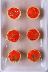 Red caviar served in shortbread tartlets topped with fresh dill on the white ceramic platter