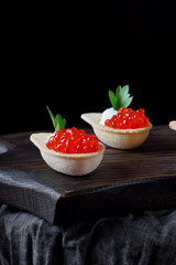 Red caviar and ricotta cheese in the spoon shaped tartlets served on the wooden board