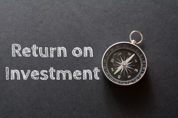 Written Return On Investment words on black background with compass