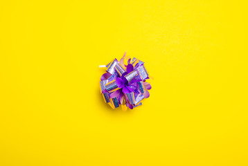 Purple decorative gift ribbon bow on yellow background, top view