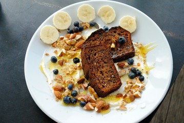 Healthy breakfast made of banana bread slices served with  yogurt, crushed almonds, maple syrup, fresh bananas and blueberries