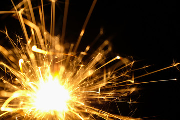 Glittering burning sparkler Bengal flame on black background.