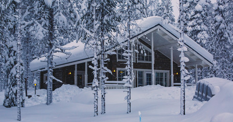 A cozy wooden cabin cottage chalet house covered in snow near ski resort in winter with the lights turn on