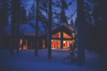 A cozy wooden cabin cottage chalet house covered in snow near ski resort in winter with the lights turn on