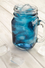 Iced blue flower tea in the glass on the white wooden background. Location vertical. Copy space. Closeup.