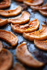 Roasted pumpkin slices seasoned with salt and herbs on a oven plate. Autumn dish closeup