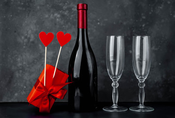 a bottle of red wine and two glasses, a gift and two hearts on a stone background for Valentines Day.
