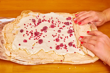 women's manicured hands wrap a roll with cream cream with raspberries on a shiny foil