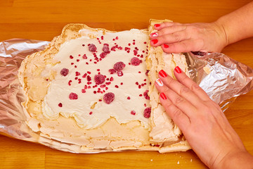 women's manicured hands wrap a roll with cream cream with raspberries on a shiny foil