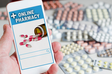 Online pharmacy. Application in your smartphone for online ordering of medicines. Phone in the man's hand close-up. Lots of pills.