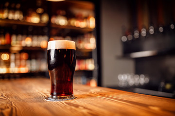 Glass with dark beer on wooden bar counter, copy space - obrazy, fototapety, plakaty