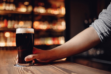 Bartender holds out glass of dark beer client behind wooden bar counter