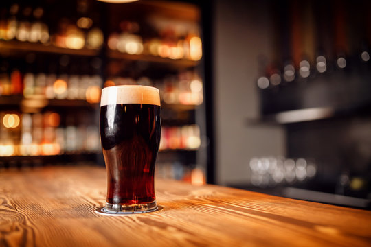 Glass with dark beer on wooden bar counter, copy space
