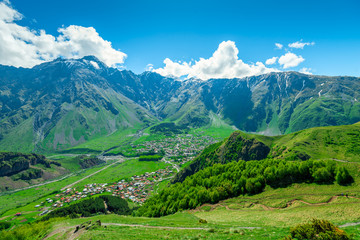 Fototapeta na wymiar View of the mountain peaks of the Caucasus and the village of Gergeti in the valley, Georgia in summer
