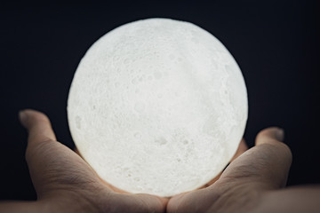A picture of a hand holding a model of the moon at night