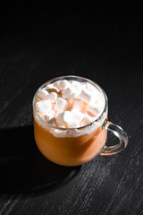 cocoa with milk and marshmallows in a transparent mug on a black background with a place for inscription