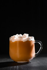 cocoa with milk and marshmallows in a transparent mug on a black background with a place for inscription
