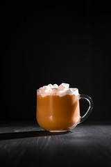 cocoa with milk and marshmallows in a transparent mug on a black background with a place for inscription