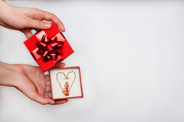 Jewelry as a gift for Valentine's Day. Holiday sale. Gold chain with red stones in the form of a heart in a box in the hands of a woman on a white background.