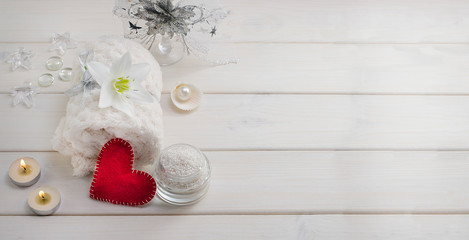 Spa treatments for Valentine's Day. White towel with flower and pearls on a white wooden background with a red heart and candles with copy space. Beauty salon