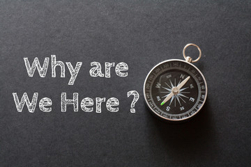 Written Why are We Here? words on black background with compass