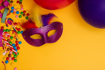 Carnival. Festive background with copy space. Carnival mask purple with feathers on a yellow background with tinsel, multi-colored sweets. Mardi Gras. Brazilian.