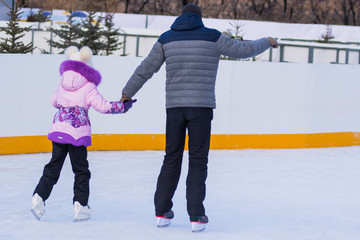 Sunny winter day. Father with daughter ride on figure skates on a outdoor skating rink. Training on...