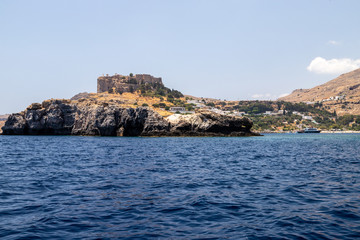 Fototapeta na wymiar View from a motor boat on the mediterranean sea at the rocky coastline and the acropolis of Lindos on the eastside of Greek island Rhodes