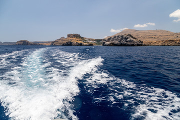 View from a motor boat on the mediterranean sea at the rocky coastline and the acropolis of Lindos on the eastside of Greek island Rhodes