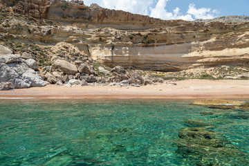 View from a motor boat on the mediterranean sea on the rocky coastline with red sand beach and clear turquoise water near Stegna on the eastside of Greek island Rhodes
