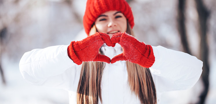 Woman making heart symbol with snowy hands in red gloves, sunny winterday, sun lights, Valentines day, Love concept.