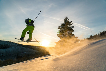 Downhill skier jumping in beautiful powder snow and sunset conditions