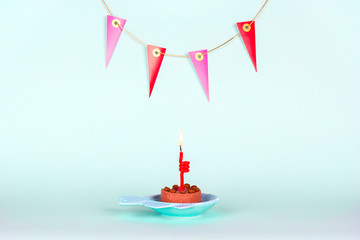 Festive cat cake with burning candle and decoration on wall on light blue background for cat's birthday party.