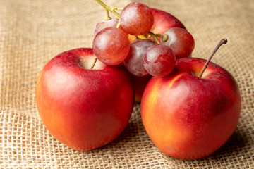 .Three red ripe apples and grapes on burlap.