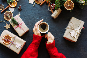 A female hand in a red sweater mug with coffee. Near Christmas decor and gift boxes.