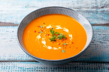 Pumpkin soup with fresh herbs in a bowl. Blue wooden background. Close up.