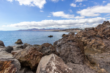 Big lava rocks on the coastline of Puerto del Carmen at Canary island Lanzarote. The sky is blue with white clouds