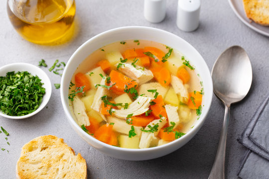 Chicken soup with vegetables in white bowl. Grey stone background. Close up.