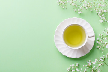 Green tea in a white cup with gypsophila flowers on green pastel background. Top view. Copy space.