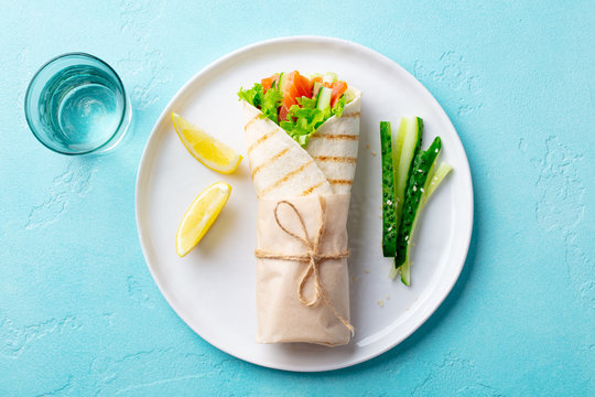 Wrap Sandwich, Roll With Salmon, Cucumber, Salad On A White Plate. Blue Background. Top View.