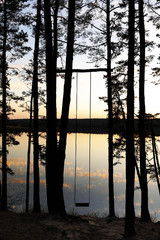 Handmade swing in the pine forest near the lake at sunset