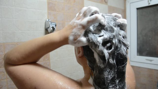 Brunette woman washing her hair with shampoo in the shower. Close-up shot from back. 