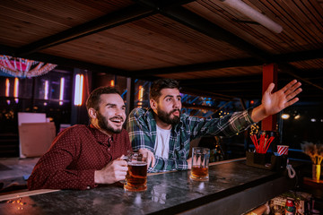 Two buddies drinking beer and watching sport competition in pub, leisure