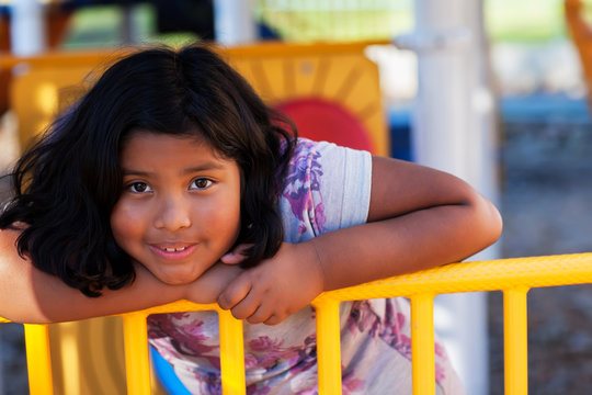 A cute hispanic girl playing in a kids area and holding on to one of the playground features.